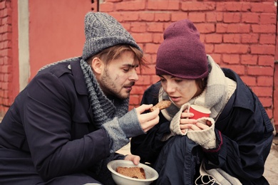 Photo of Poor young couple with bread on dirty street