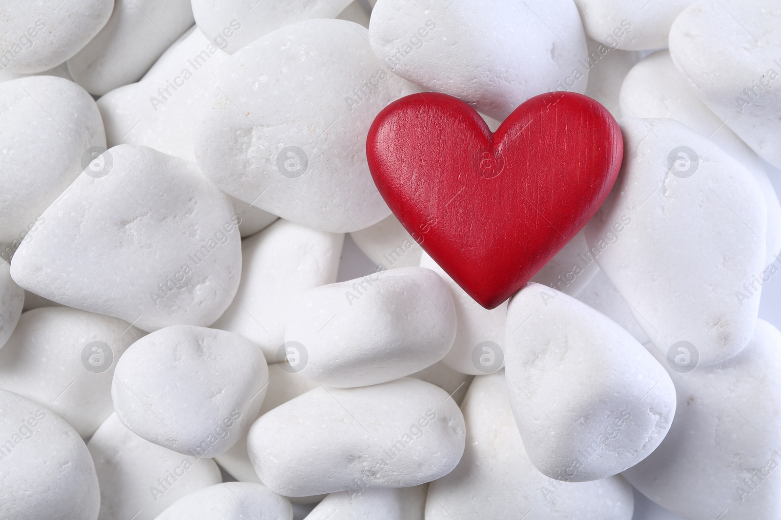 Photo of Decorative heart on white pebble stones, top view