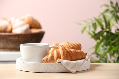 Plate of fresh croissants served with cup of coffee on wooden table indoors. French pastry