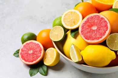 Different fresh citrus fruits and leaves in bowl on light table, closeup