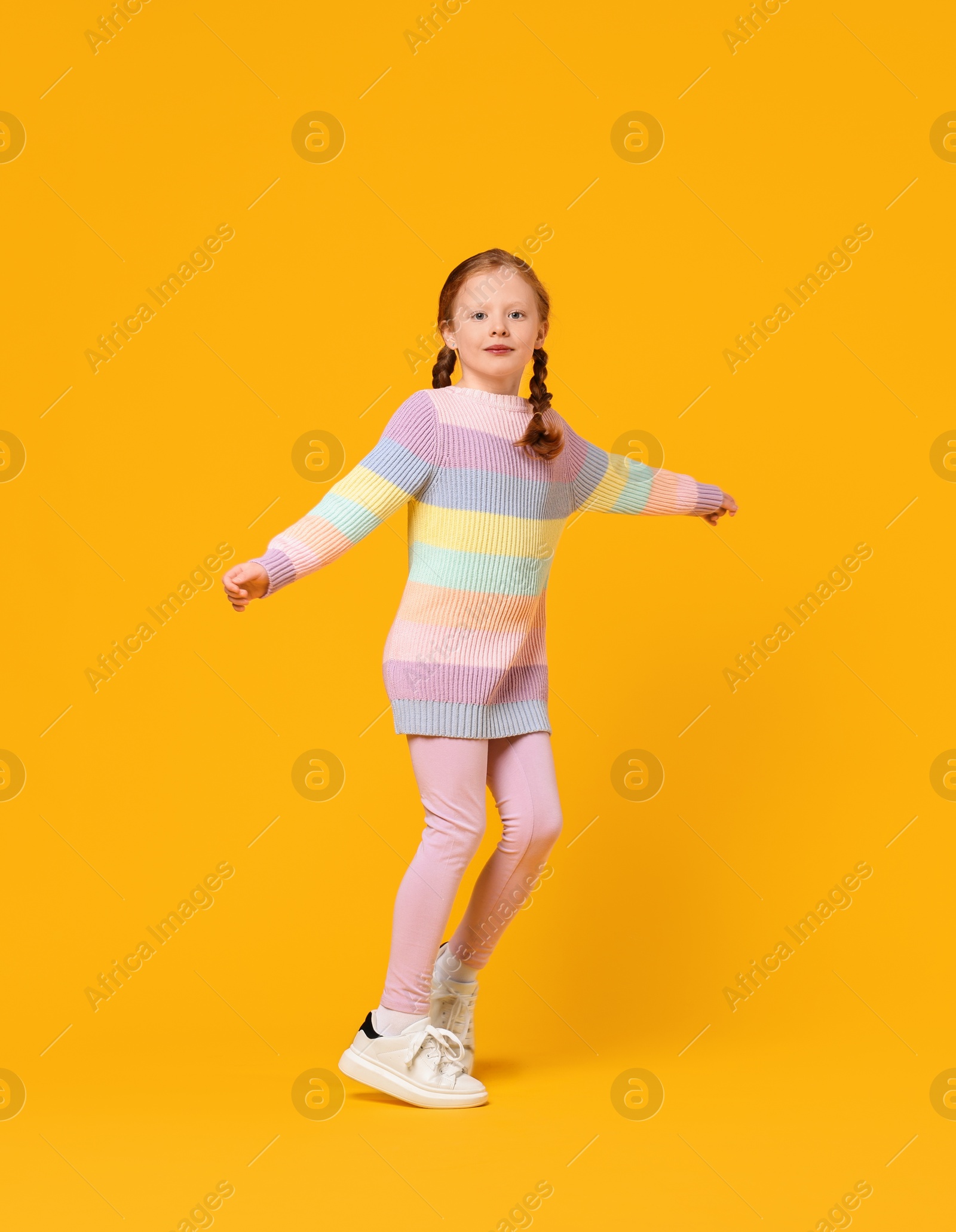 Photo of Cute little girl dancing on orange background