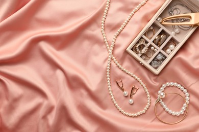 Photo of Box with luxurious pearl jewelry on pink fabric, flat lay. Space for text