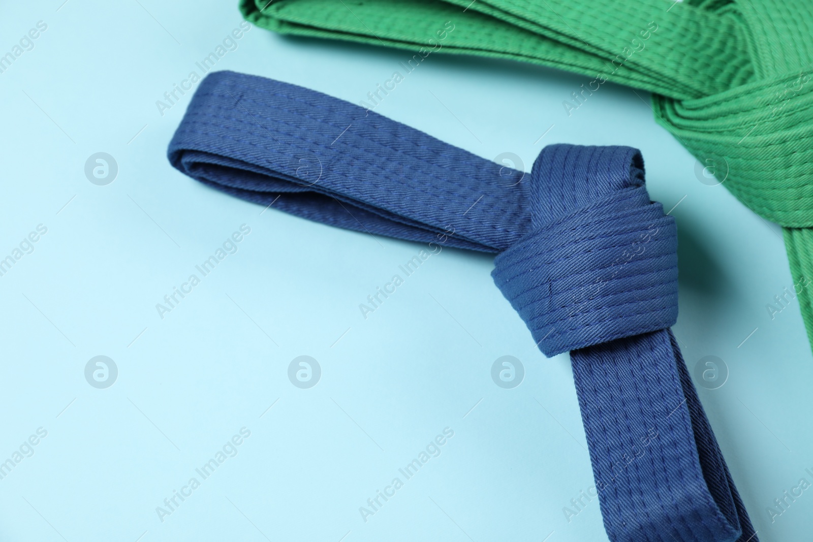 Photo of Colorful karate belts on light blue background, space for text