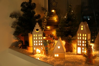 Photo of Christmas atmosphere. Beautiful glowing houses, fir trees and toys on window sill indoors