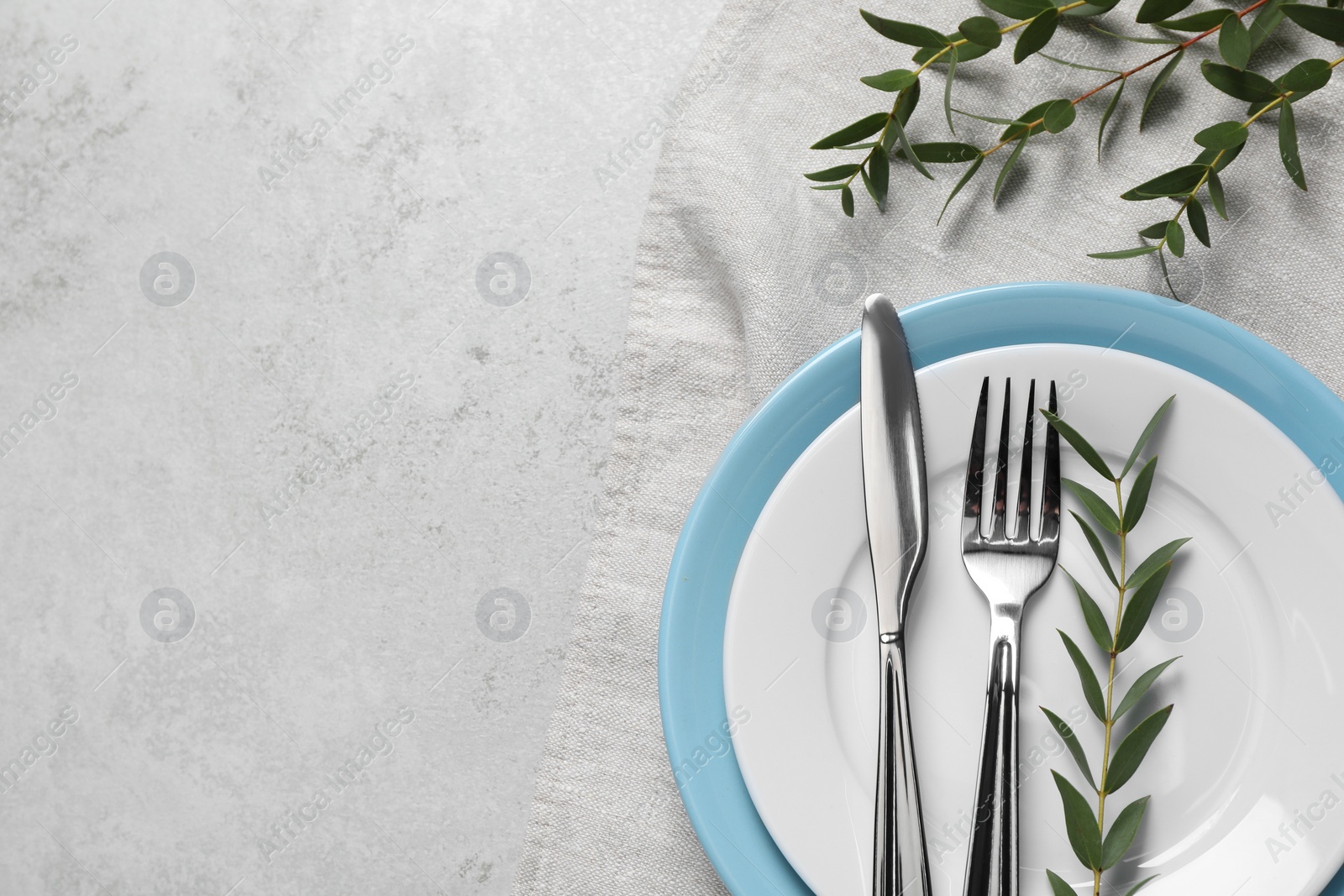 Photo of Stylish setting with cutlery and eucalyptus leaves on light grey table, flat lay. Space for text