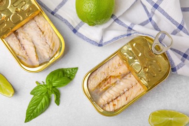 Open tin cans with mackerel fillets, lime and basil on grey table, flat lay