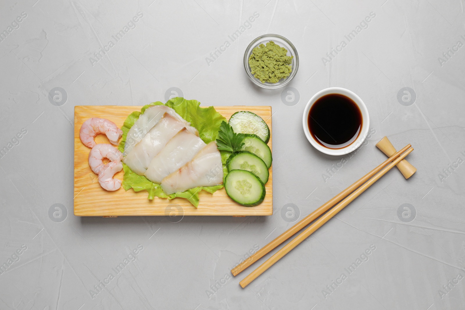 Photo of Sashimi set served with cucumber, lettuce, soy sauce and vasabi on light grey table, flat lay