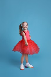 Photo of Cute little girl in tutu skirt dancing on light blue background