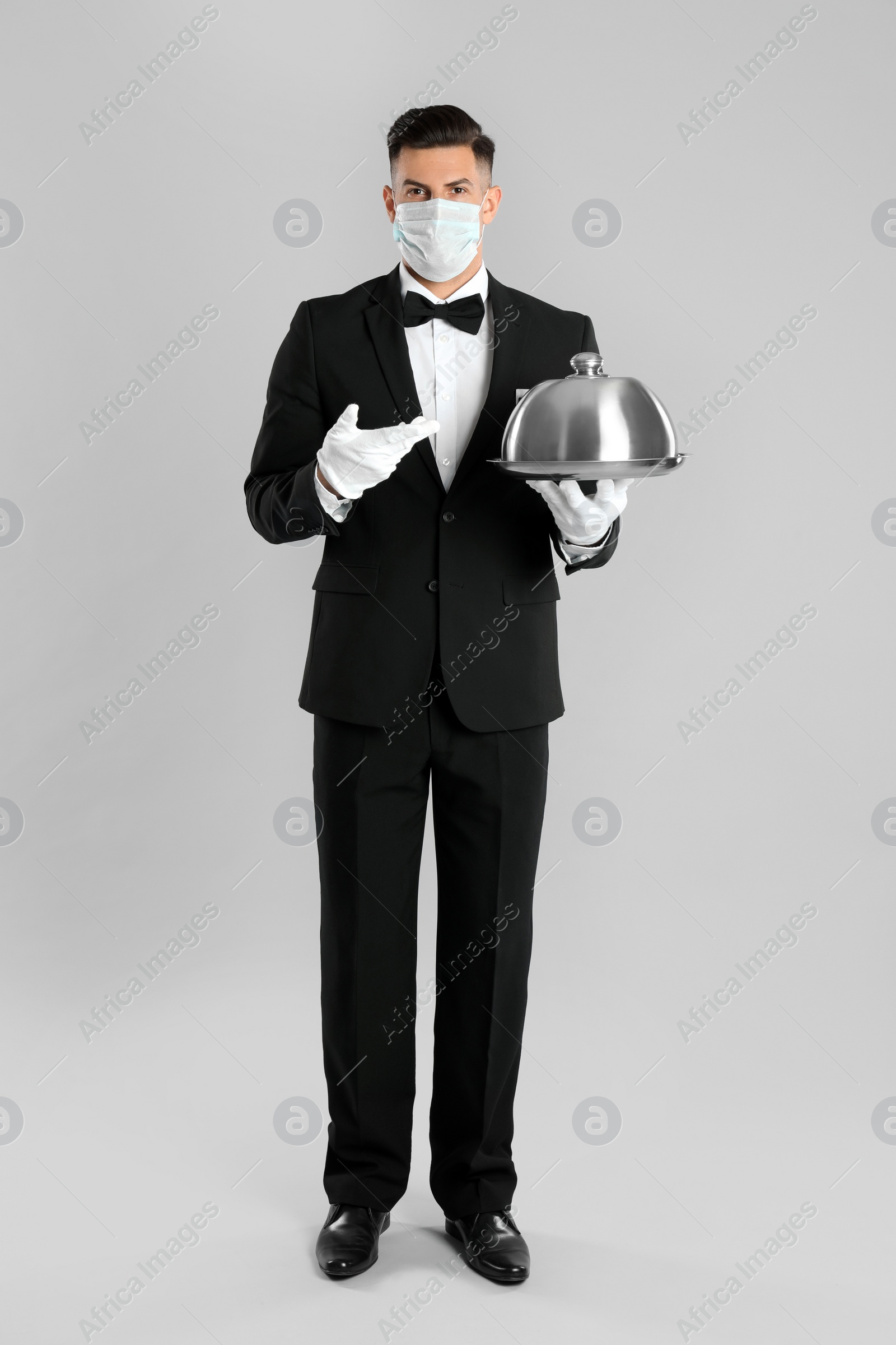 Photo of Waiter in medical face mask holding tray on light grey background