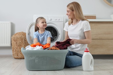 Mother and daughter taking out dirty clothes from basket in bathroom