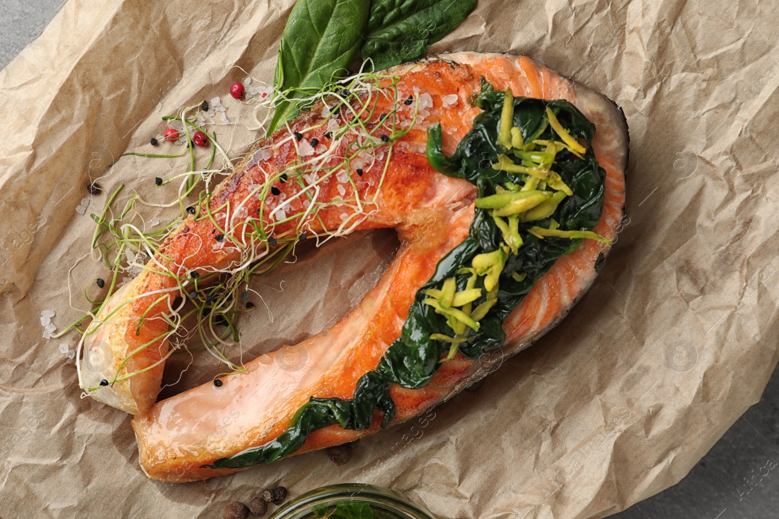 Photo of Tasty salmon with spinach on parchment, closeup