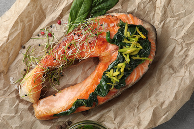 Photo of Tasty salmon with spinach on parchment, closeup