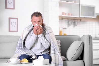 Photo of Man suffering from cough and cold on sofa at home. Space for text