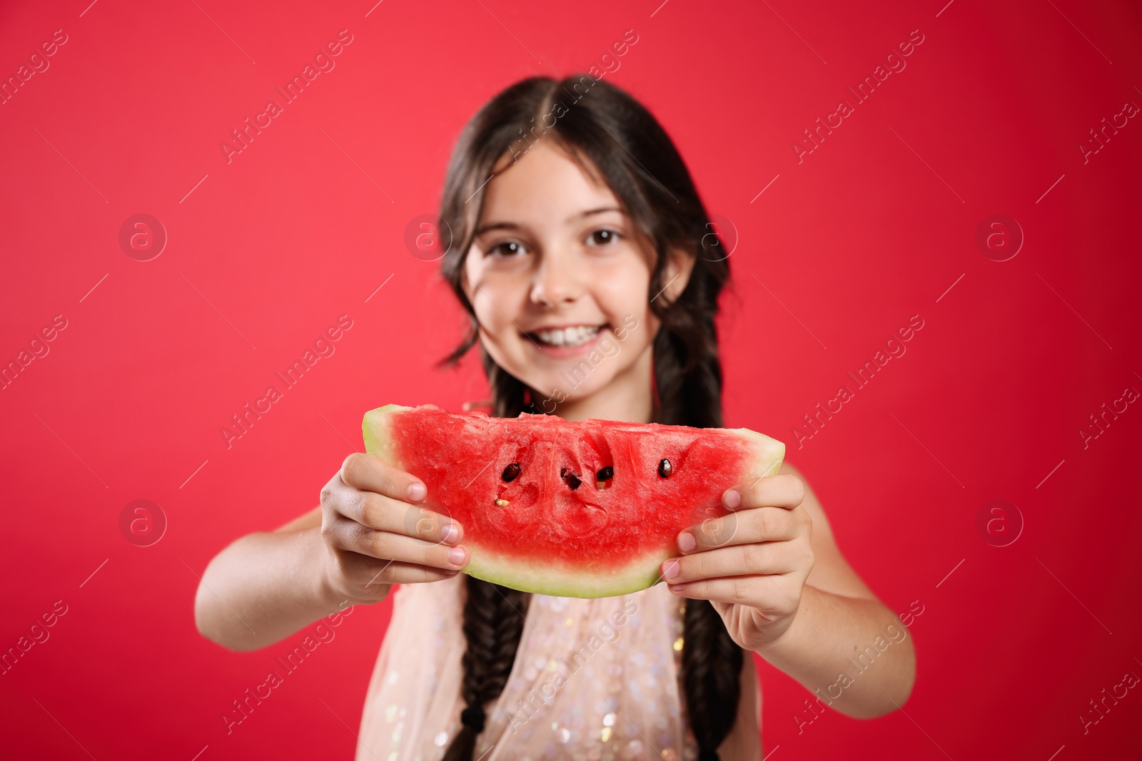 Photo of Cute little girl against red background, focus on hands with watermelon