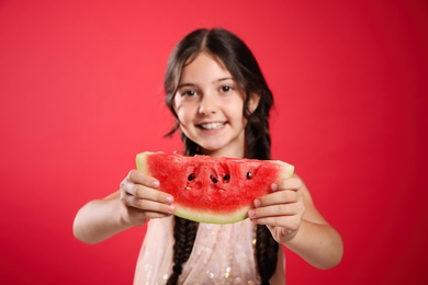 Photo of Cute little girl against red background, focus on hands with watermelon