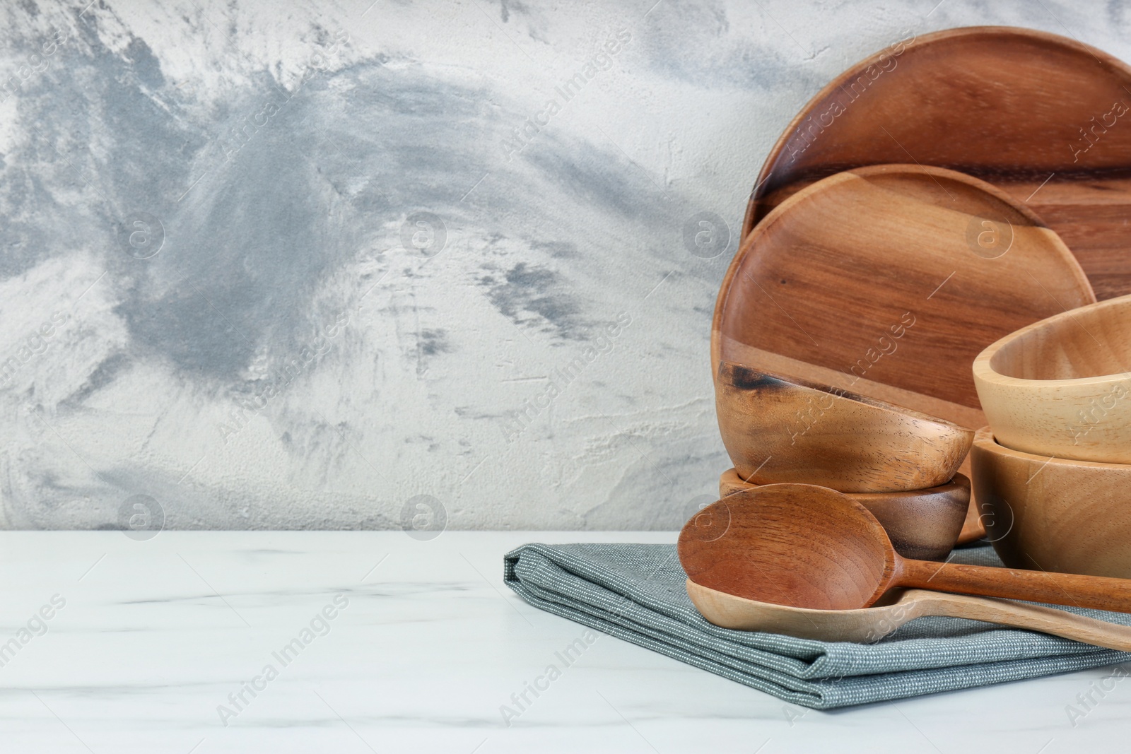 Photo of Set of wooden tableware on white marble table against textured wall. Space for text