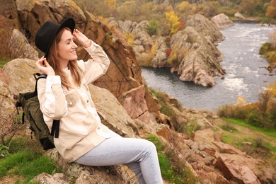 Woman with travel backpack sitting on steep cliff near mountain river