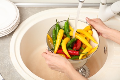 Photo of Woman washing chili peppers over sink, closeup