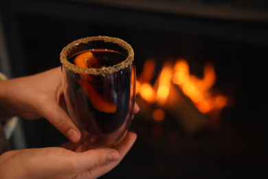 Photo of Woman with tasty mulled wine near fireplace indoors, closeup