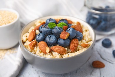 Bowl of delicious cooked quinoa with almonds and blueberries on white textured table, closeup