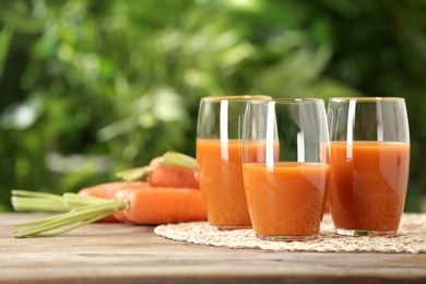 Photo of Glasses of juice and carrots on wooden table against blurred background, space for text