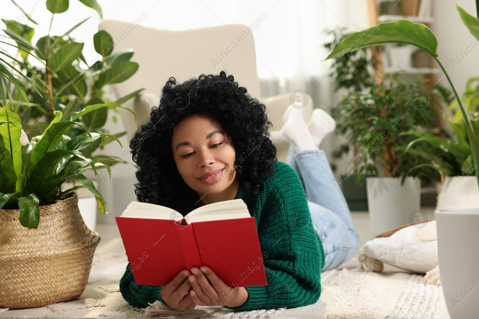 Photo of Relaxing atmosphere. Woman reading book surrounded by potted houseplants at home