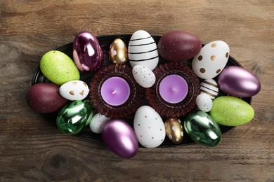 Photo of Many beautifully decorated Easter eggs and scented candles on wooden table, top view