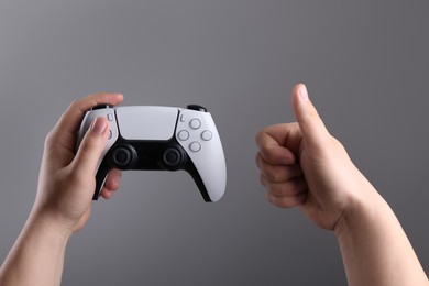 Photo of Woman using wireless game controller and showing thumbs up on grey background, closeup