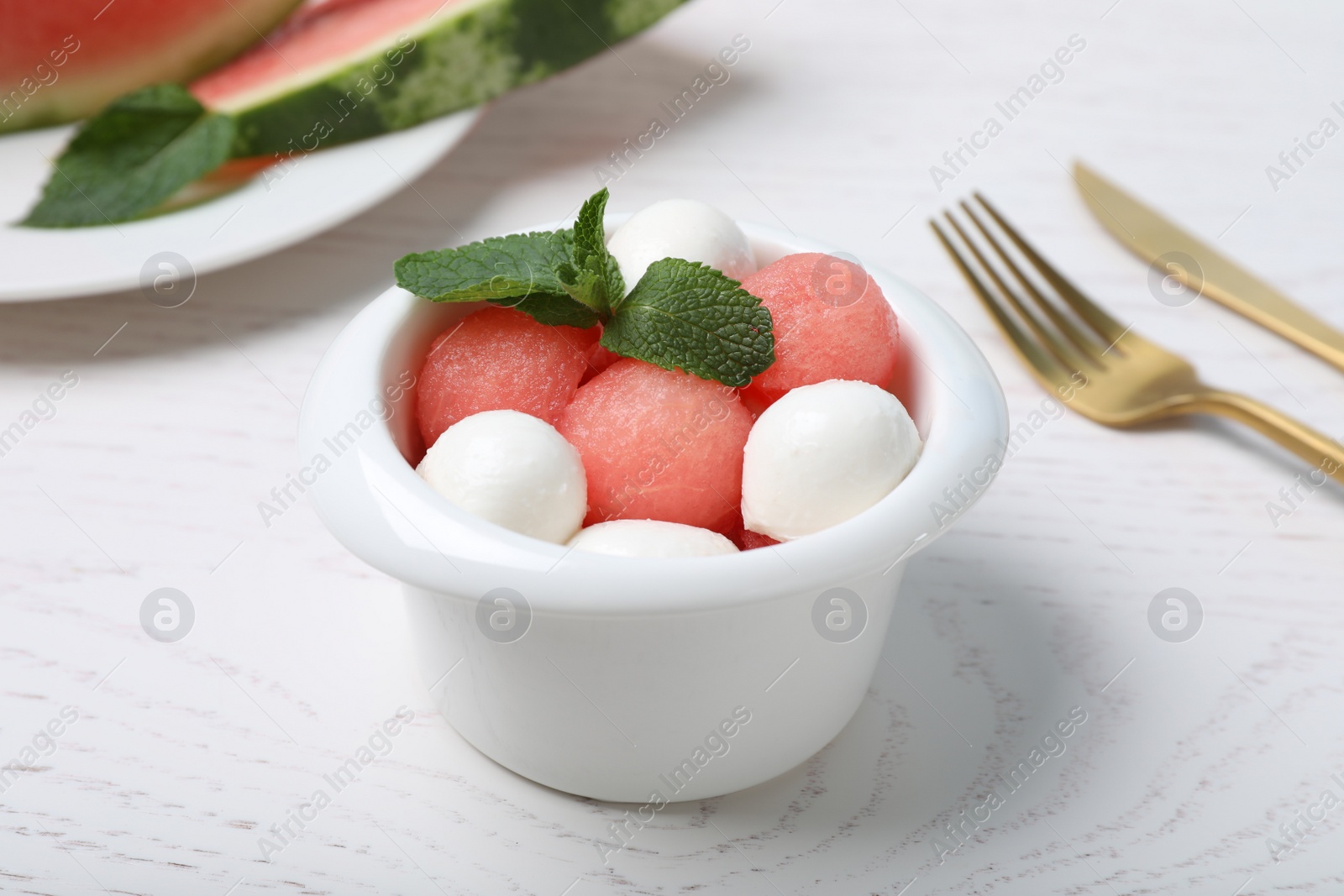 Photo of Delicious salad with watermelon balls, mint and mozzarella served on white wooden table, closeup