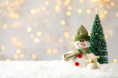 Snowman toy and Christmas ball on snow against blurred festive lights. Space for text