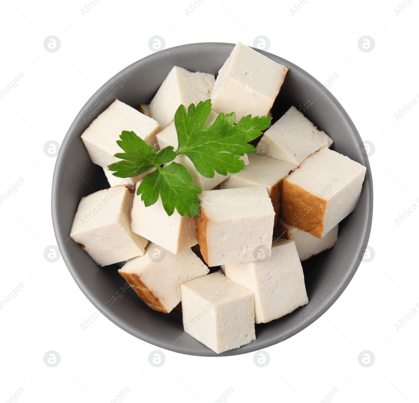 Photo of Bowl of delicious smoked tofu cubes with parsley isolated on white, top view