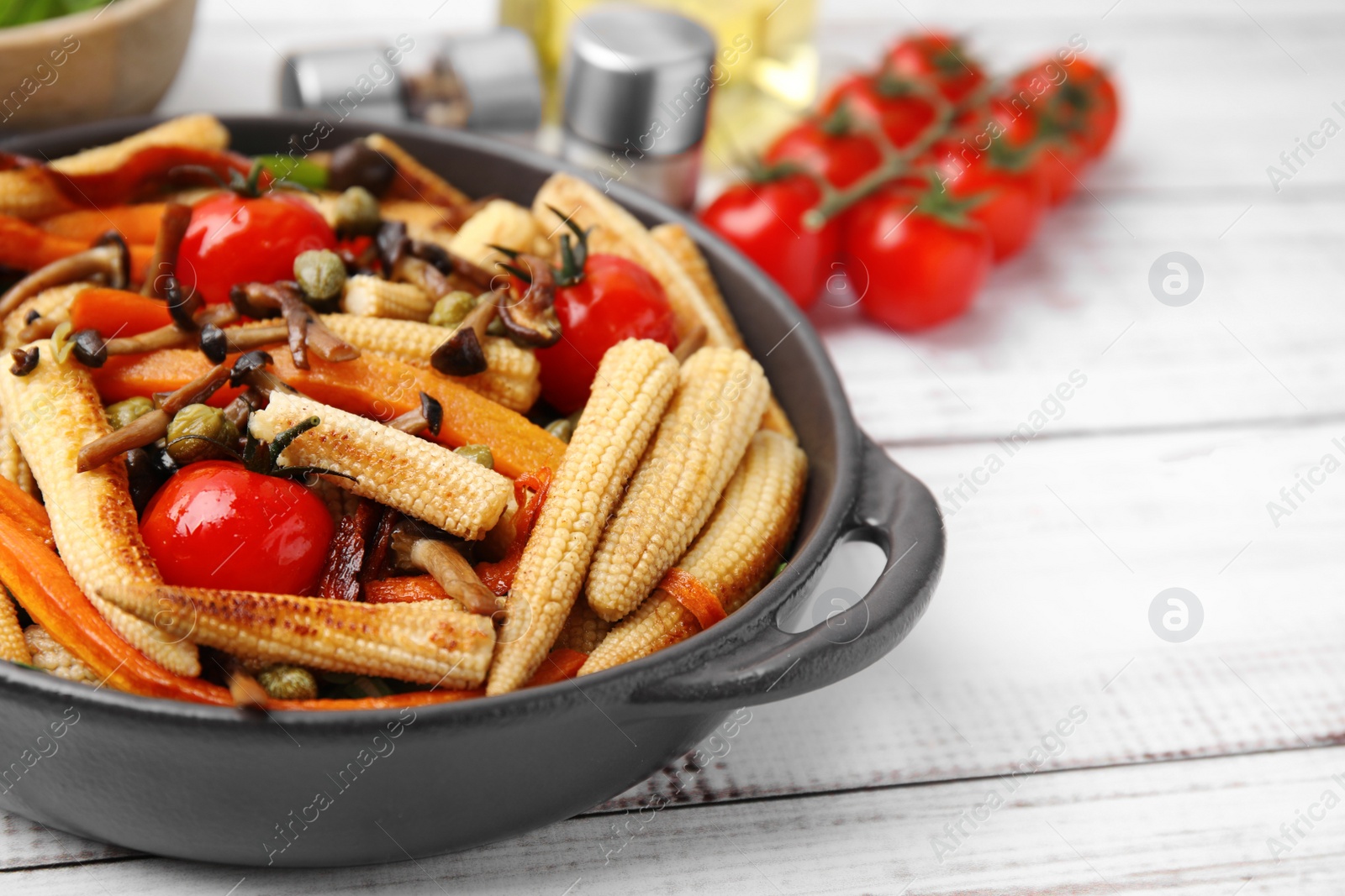 Photo of Tasty roasted baby corn with tomatoes, capers and mushrooms on white wooden table, closeup. Space for text