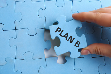 Image of Woman putting light blue puzzle piece with phrase PLAN B, closeup