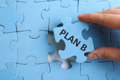 Woman putting light blue puzzle piece with phrase PLAN B, closeup