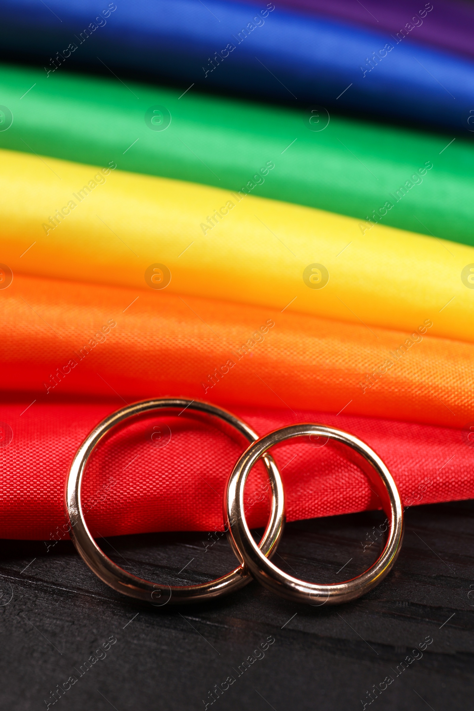 Photo of Rainbow LGBT flag and wedding rings on black wooden background