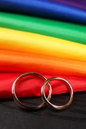 Rainbow LGBT flag and wedding rings on black wooden background