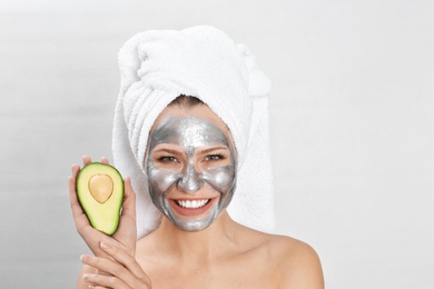 Photo of Beautiful woman holding avocado near her face with silver mask against light background. Space for text