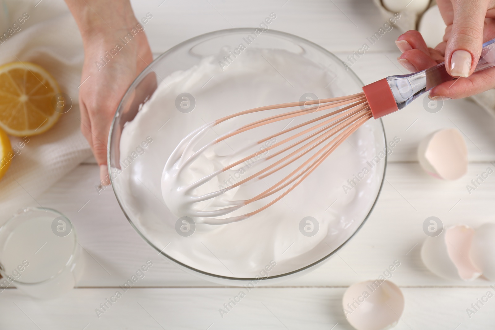 Photo of Woman making whipped cream with whisk at white wooden table, above view