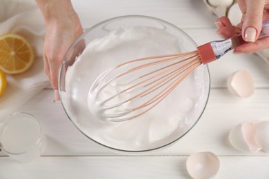 Photo of Woman making whipped cream with whisk at white wooden table, above view