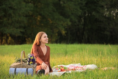 Photo of Beautiful young woman with picnic basket sitting on blanket in park