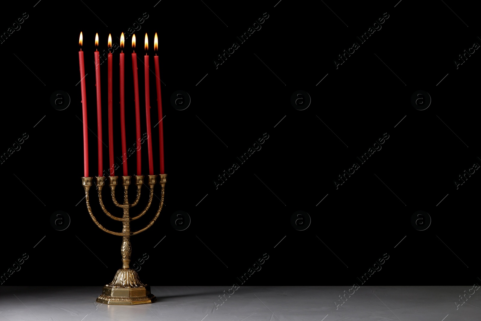 Photo of Golden menorah with burning candles on table against black background, space for text