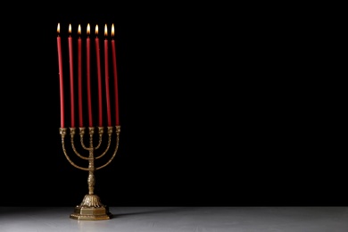 Photo of Golden menorah with burning candles on table against black background, space for text