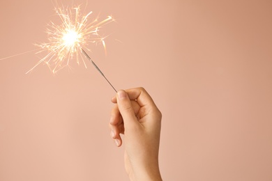 Photo of Woman holding bright burning sparkler on beige background, closeup