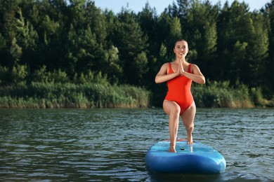 Young woman practicing yoga on light blue SUP board on river