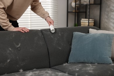 Photo of Pet shedding. Man with lint roller removing dog's hair from sofa at home, closeup