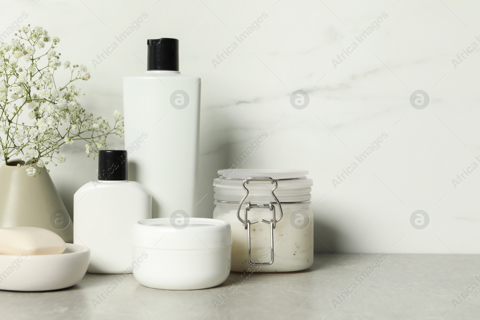 Photo of Bath accessories. Personal care products and gypsophila flowers in vase on gray table near white marble wall, space for text