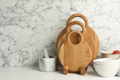 Photo of Wooden cutting boards, mortar with pestle and bowls on white table near marble wall, space for text