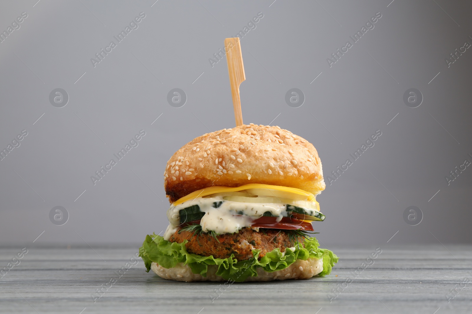 Photo of Delicious vegetarian burger on grey wooden table