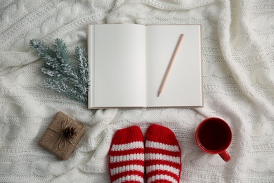 Photo of Woman with cup of hot winter drink and notebook on knitted plaid, top view. Cozy season