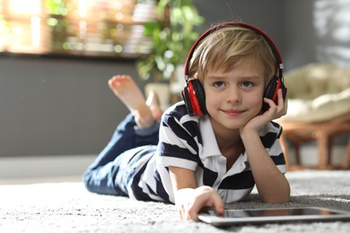 Photo of Cute little boy with headphones and tablet listening to audiobook at home